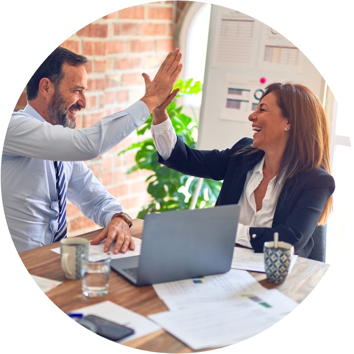 Twee collega's aan een kantoortafel geven elkaar een high-five bij hun laptop - het moment waarop een verandering vasthoudt.
